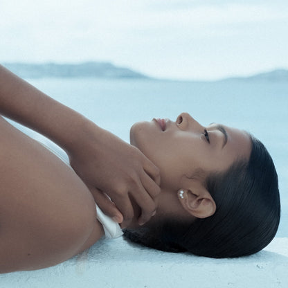 Woman lying on a white wall with a blurred sea background, wearing Calliadne earrings made of 3 freshwater pearls