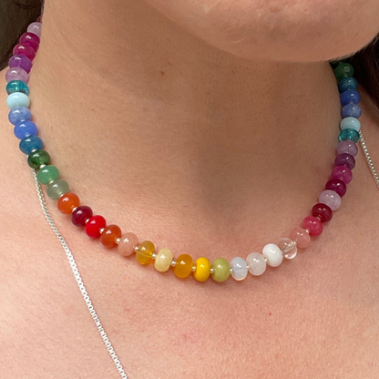 A close-up of a person's neck and chest wearing a rainbow-colored beaded chakra necklace with a silver chain.