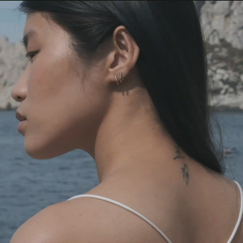 Video of a model who is wearing the Jasper earrings, part of the Icons jewellery collection, designed by Aurore Havenne. It is a gold plated silver pair of earrings.