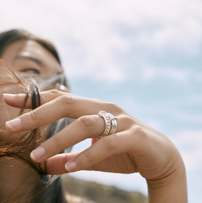 Outdoor photo of a model. Her hand is in the foreground, wearing the Ellis ring, a 2mm ring and a twisted ring.