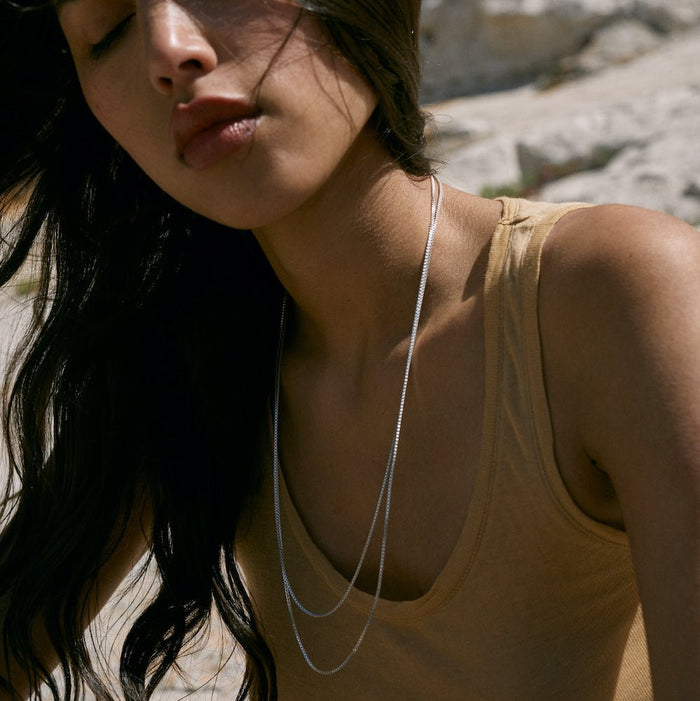 Outdoor photo of a model wearing the Sacha silver necklace. The model's neckline is clear to show off the Sacha necklace.