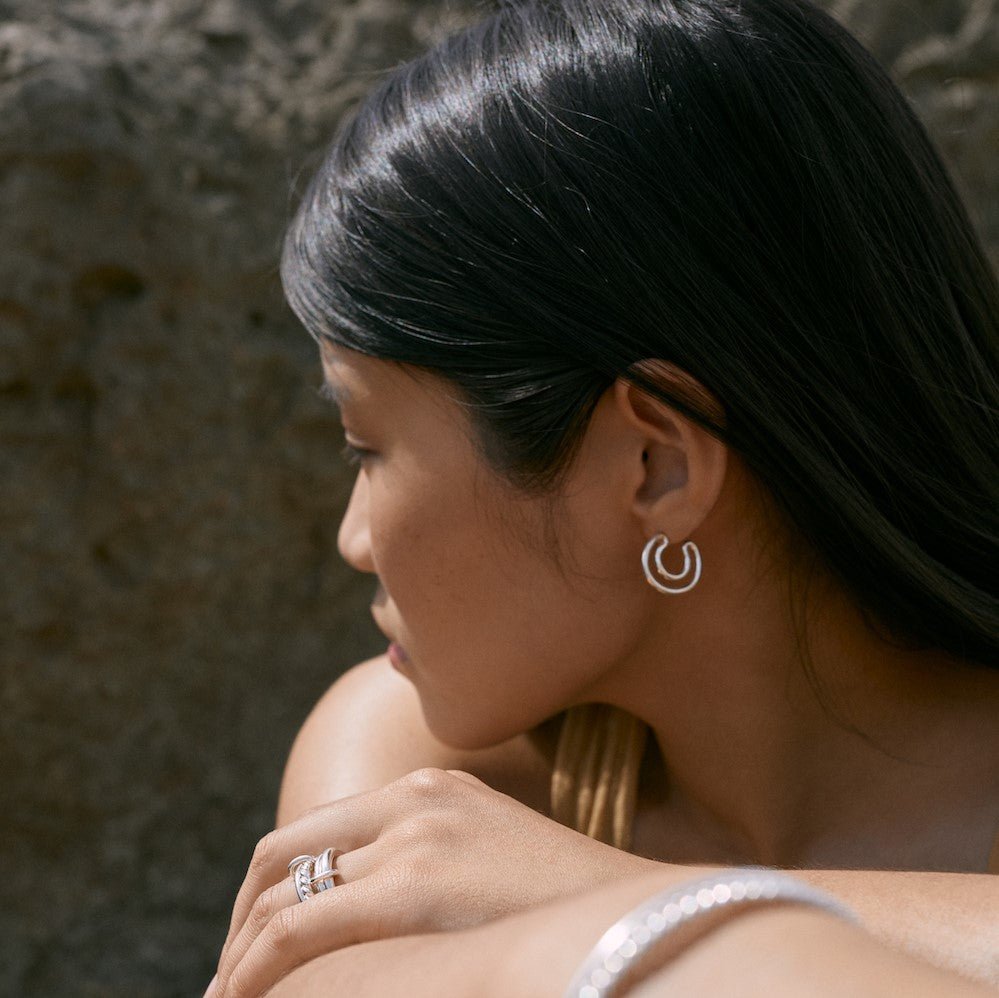 Outdoor photo of a model wearing the silver Artémis earrings. She is also wearing the Ellis ring and the Billie 2mm ring.